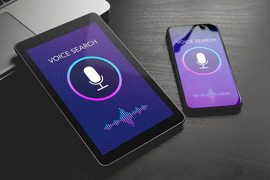 Tablet and smartphone displaying 'Voice Search' screens with microphone icons and soundwave graphics, showcasing voice search technology on both devices.