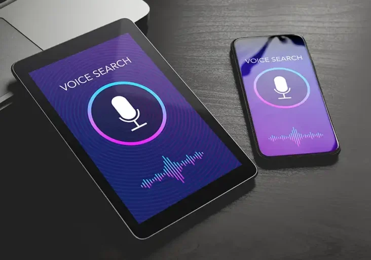 Tablet and smartphone displaying 'Voice Search' screens with microphone icons and soundwave graphics, showcasing voice search technology on both devices.